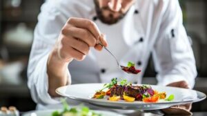 chef carefully spoons red sauce onto plate food food is arranged beautifully plate includes steak vegetables greens 14117 526687