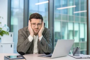 close up portrait young male office worker sitting his desk head resting his hands looking bored tired 391551038