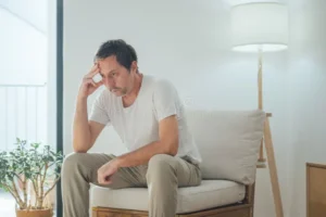 portrait sad depressed man sitting alone living room looking down regret emotional pain quiet low light home 418013117
