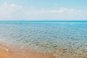 clear turquoise sea smooth stones visible beneath shallow water calm shoreline under bright sky distant mountains 398216858