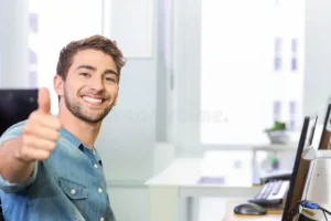 man sitting office desk wearing denim shirt giving thumbs up near computer setup copy space professional workspace modern 387759358